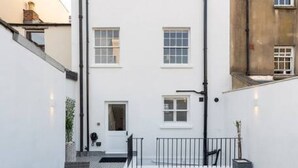 A courtyard with a dining table and chairs, a small garden, and a white building with multiple windows and a chimney. - Gloucester Place Townhouse + Hot Tub (Cheltenham)