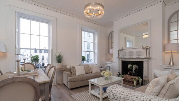 A spacious living room with a fireplace, large windows, and a chandelier.