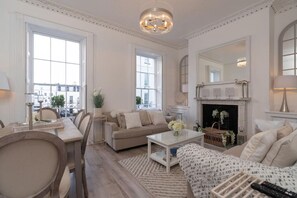 A spacious living room with a fireplace, large windows, and a chandelier.