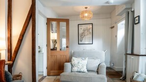 A cozy living room with a grey sofa, a wooden door, and a hanging light fixture. - Windsor Cottage - Bolthole in the heart of CN (Chipping Norton)