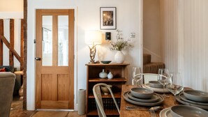 A dining area with a wooden table set for four, a wooden door, and a bookshelf with decorative items. - Windsor Cottage - Bolthole in the heart of CN (Chipping Norton)