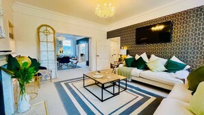 Een woonkamer met een bank, salontafel en een aan de muur bevestigde televisie. Achtergrond is een eethoek met een tafel en stoelen.
