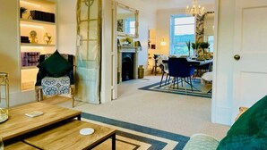 Een ruime woonkamer met een eettafel en stoelen, een bank en een decoratieve spiegel.