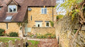 A stone house with a sloped roof, a wooden fence, and a garden with fallen leaves. - Granary Cottage - Luxury Barn Conversion (Weston Subedge)