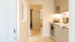 A narrow hallway leading to a kitchen with a herringbone floor pattern, a stove, and a kettle on the counter. - Bright & Airy 2BD - 10 mins walk into Centre (Cheltenham)
