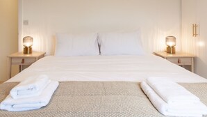 A neatly made bed with white linens, two bedside tables with lamps, and folded towels on the bed. - Bright & Airy 2BD - 10 mins walk into Centre (Cheltenham)