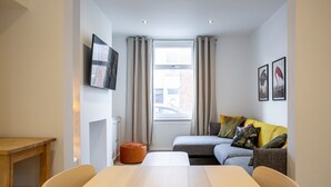 A compact living space with a sofa, a dining table, and a TV mounted on the wall. - Bright & Airy 2BD - 10 mins walk into Centre (Cheltenham)