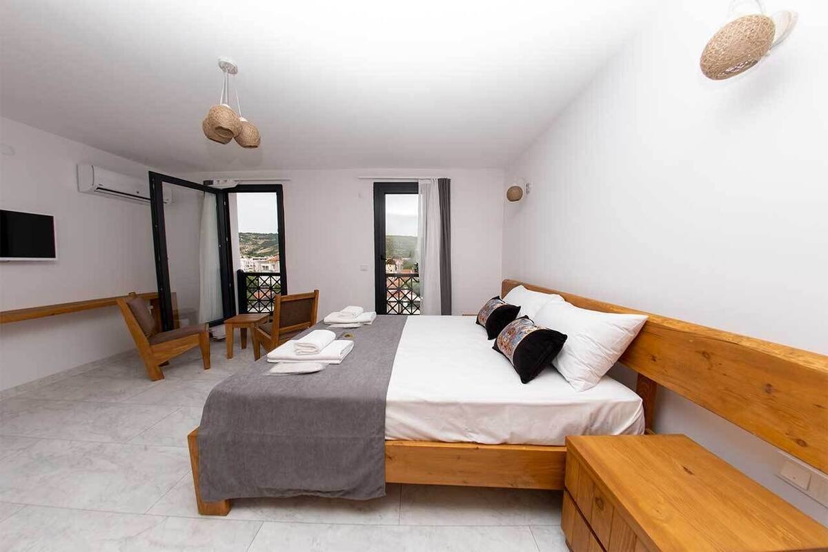 A bedroom with a bed, bedside tables, a chair, a TV, and a balcony with a view.