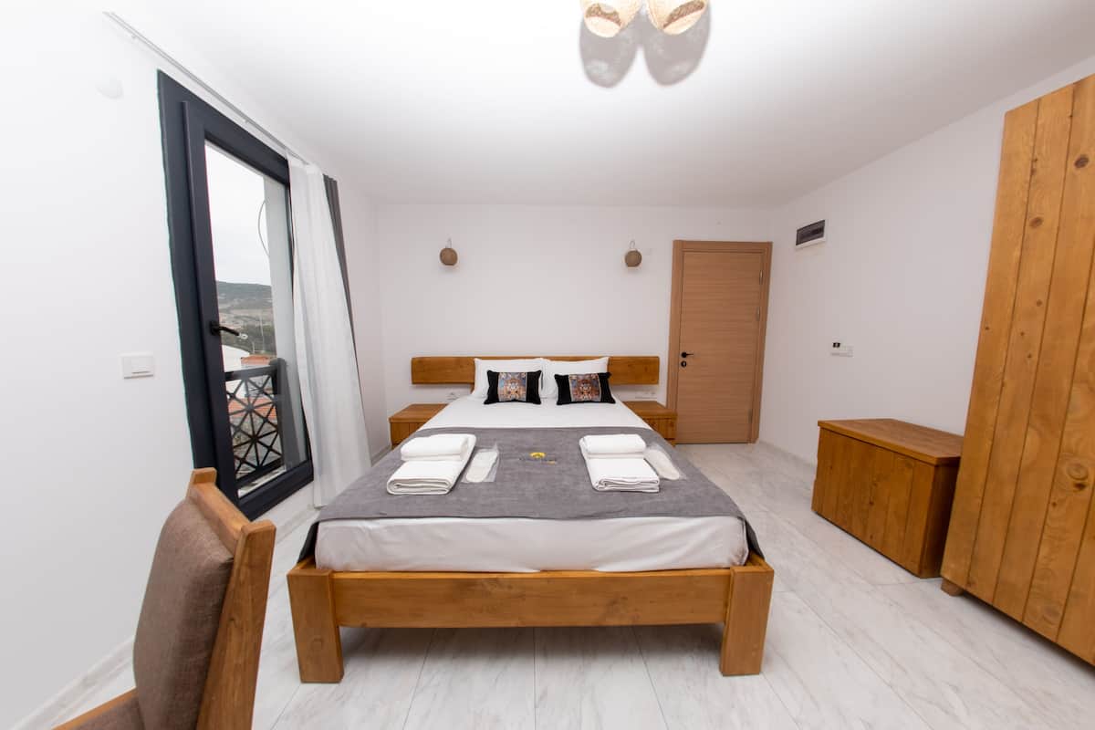 A bedroom with a wooden bed, a balcony door, a wardrobe, and a small wooden nightstand.