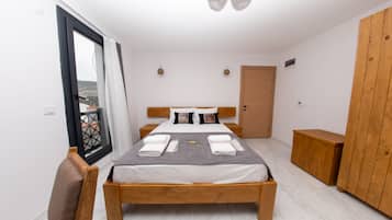Un dormitorio con cama de madera, puerta al balcón, armario y una mesita de noche de madera.