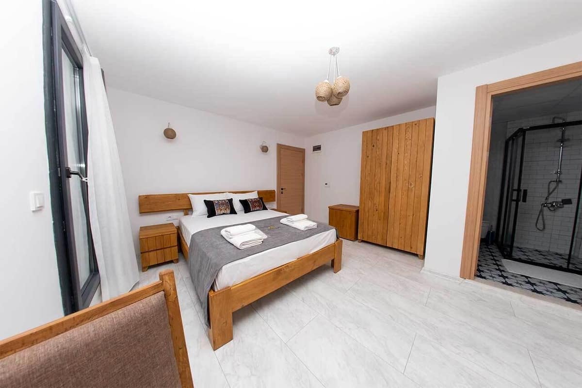 A modern bedroom with a wooden bed, bedside tables, a wardrobe, and a shower area.