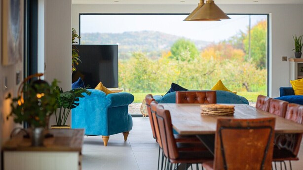 Een moderne eetruimte met een groot raam, blauwe gestoffeerde stoelen en een houten eettafel.