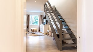 A modern interior with a wooden staircase, a window with curtains, a small bench, and a desk with a lamp. - Modern 2 BD w Garden in the Heart of Tetbury (Tetbury)