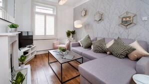 Een moderne woonkamer met een grijze bank, een salontafel en een televisie op een witte kast.