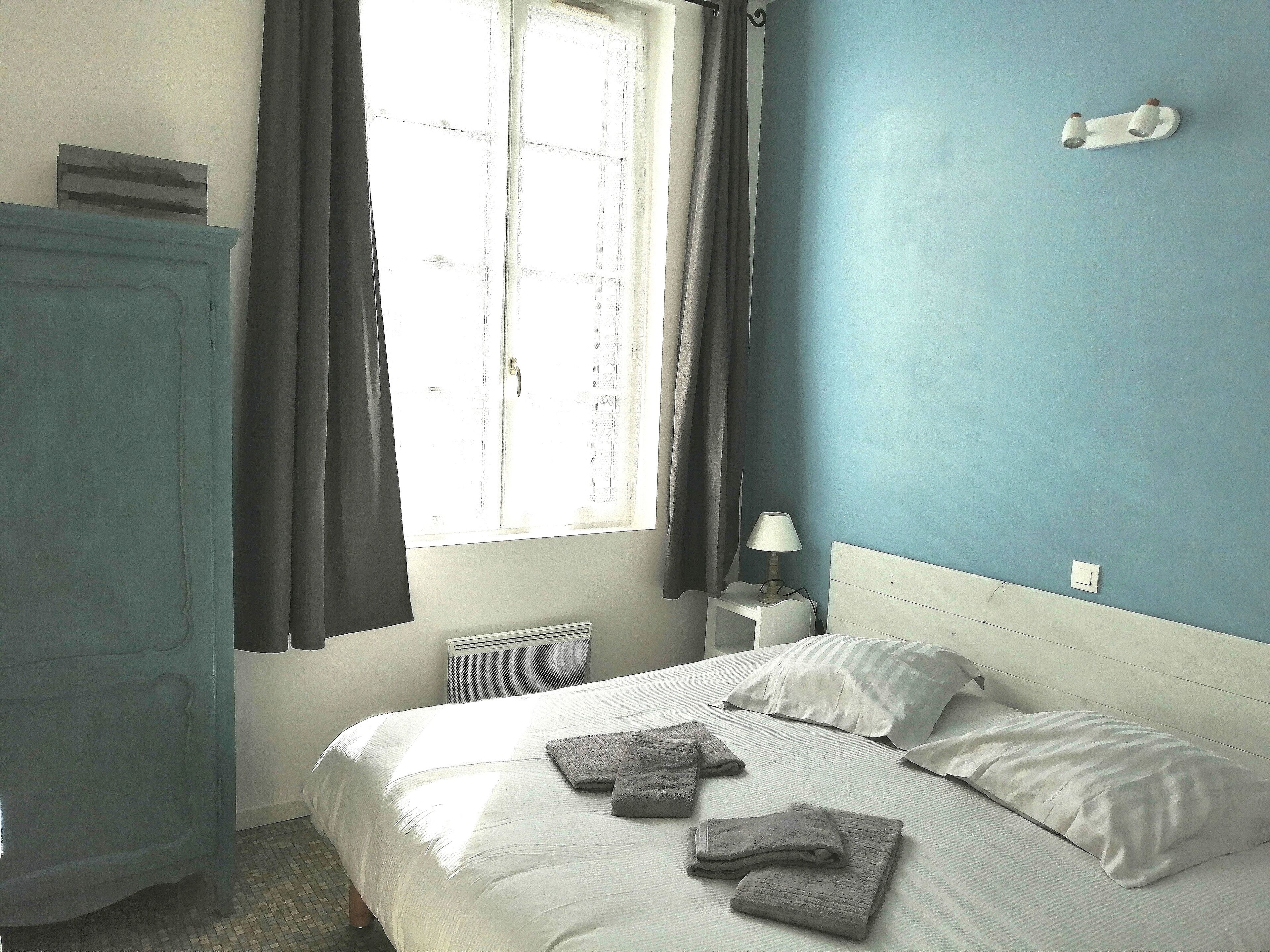 A bedroom with a bed, a nightstand, a lamp, a window with curtains, and a wardrobe.