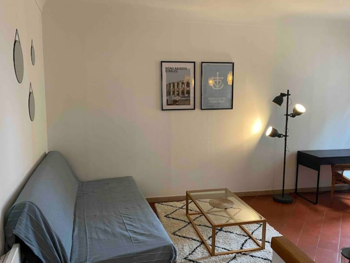 Una habitación con un sofá gris, una mesa de centro de vidrio, un tapete estampado y dos cuadros en la pared.