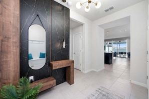 A modern interior with a dark marble wall, a round mirror, a wooden bench, and a view to a balcony with outdoor seating.