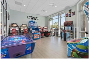 Un área de juegos interior con varias máquinas de arcade, una mesa de ping pong y un cartel que dice 'Gaming Zone'.