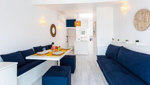 A modern living room with a dining area, featuring a sofa, a dining table set with plates and glasses, and a kitchen in the background. - MAISON BLEUE AP4362 By Riviera Holiday Homes (Villefranche-sur-Mer)