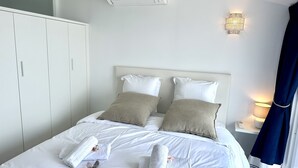 A neatly made bed with white and beige linens, a set of towels, and toiletries on a white bedspread. - MAISON BLEUE AP4362 By Riviera Holiday Homes (Villefranche-sur-Mer)