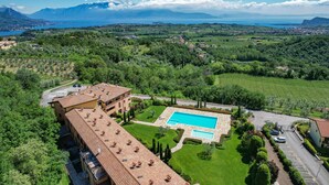 A hotel with a swimming pool, surrounded by lush greenery and a view of mountains and a lake.