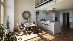 A modern kitchen with a central island, a dining area with a round mirror, and a staircase leading to an upper level.