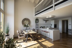 Een moderne keuken met een centraal eiland, een eetgedeelte met een ronde spiegel, en een trap die naar een hoger gelegen verdieping leidt.