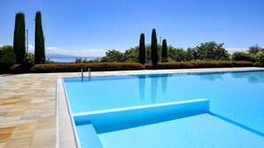 A rectangular swimming pool with a tiled deck, surrounded by neatly trimmed hedges and tall, slender trees.