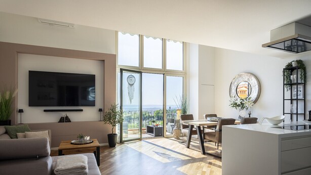 A modern living room with a flat-screen TV, a sofa, a dining area with a table and chairs, and a kitchen with a white countertop.