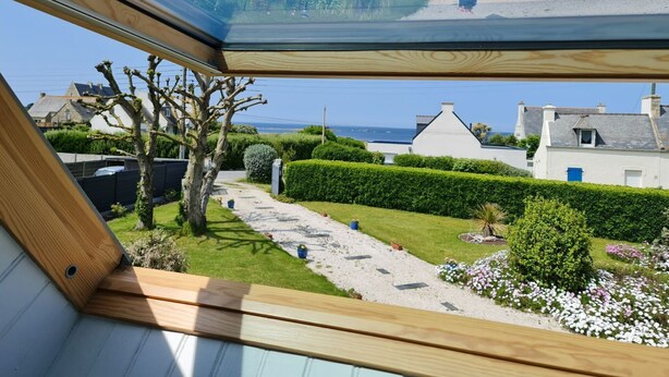 A view from a window overlooking a garden with a pathway, neatly trimmed hedges, and a white building with a blue door.