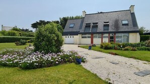 A two-story house with a gravel driveway and a garden with flowers.