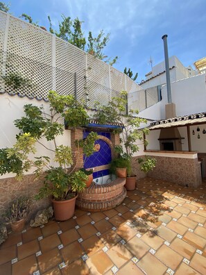 Une cour avec une fontaine aux carreaux bleus, des plantes en pot et un espace barbecue.