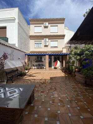 A courtyard with a tiled floor, a bench, potted plants, and a building with a tiled roof and windows. - Casa Hemingway - Marbella Old Town (Marbella)