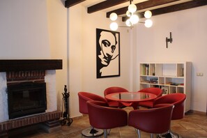 Un salon avec une cheminée, des fauteuils rouges, une table en verre et une bibliothèque.