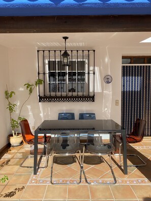 A dining area with a glass table, metal chairs, a potted plant, and a decorative wall piece. - Casa Hemingway - Marbella Old Town (Marbella)