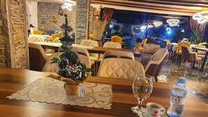 A restaurant interior with wooden tables, cushioned chairs, and a Christmas tree centerpiece.