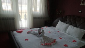 A neatly made bed with white linens and red rose petals arranged in a swan shape.