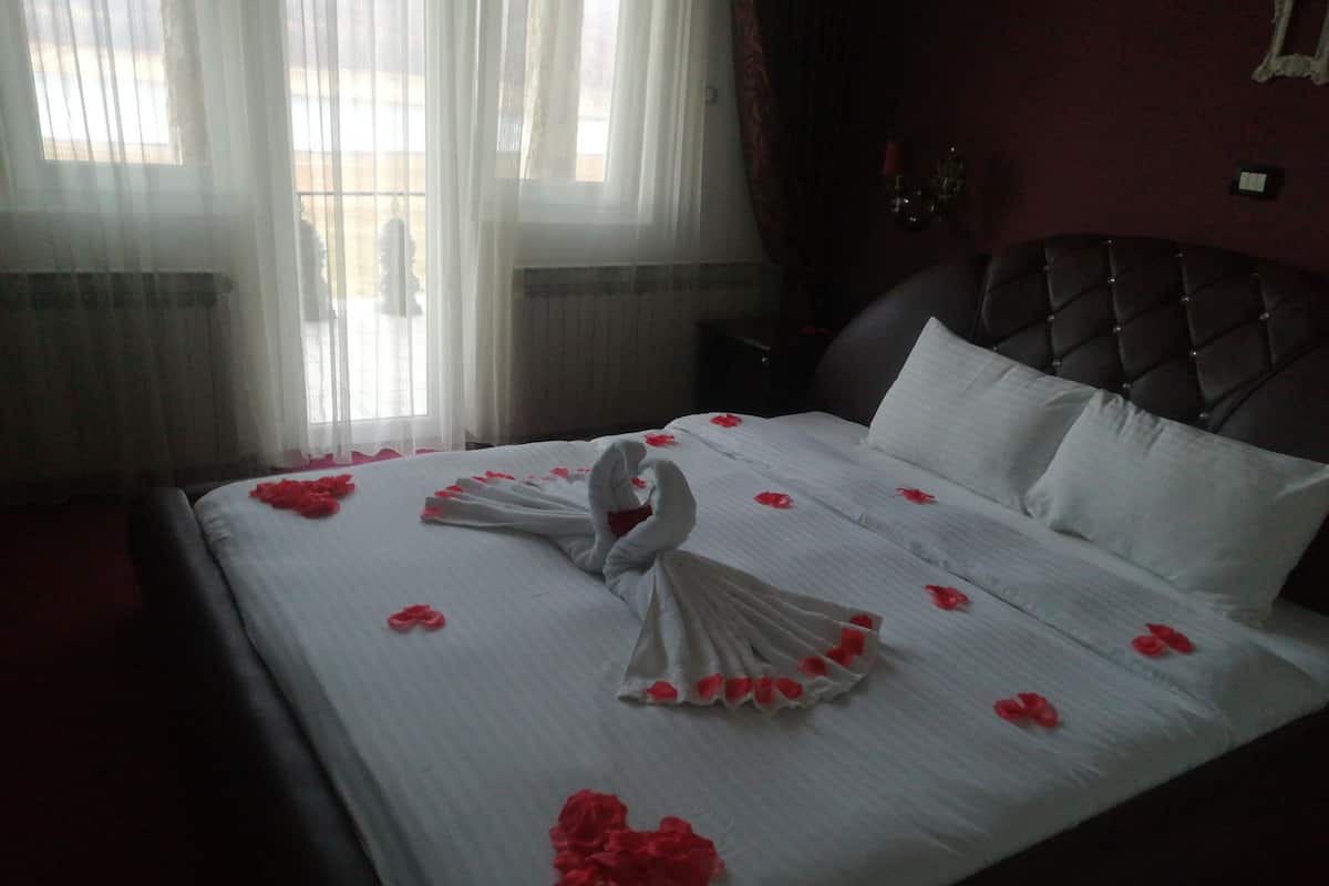 A neatly made bed with white linens and red rose petals arranged in a swan shape.