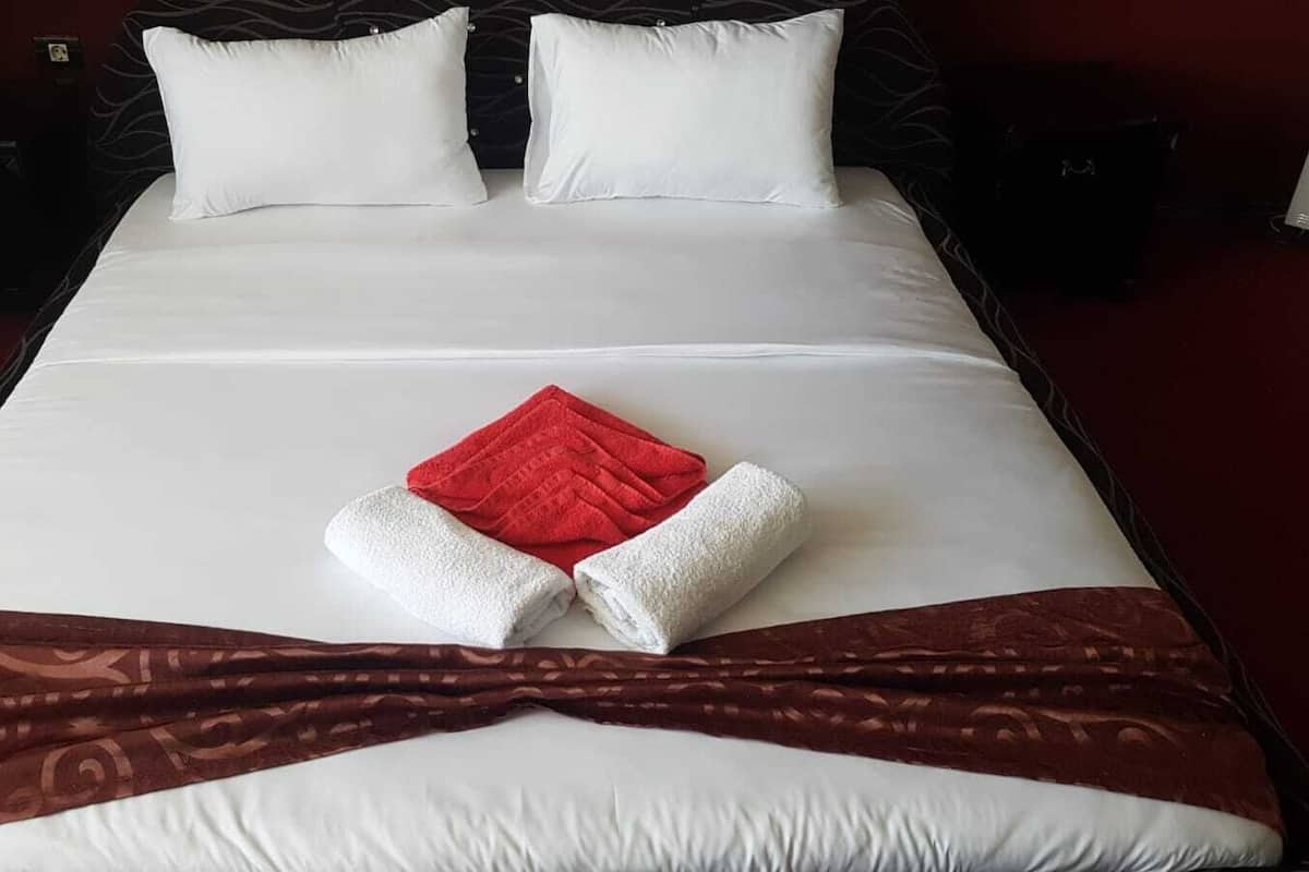 A neatly made bed with white and red linens, a brown decorative runner, and two white pillows.