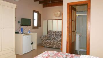 Un dormitorio con cama, escritorio con computadora, silla, armario y baño visible a través de una puerta abierta.