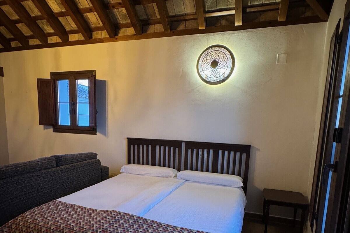 A bedroom with a bed, a sofa, a small table, and a wall-mounted light fixture.