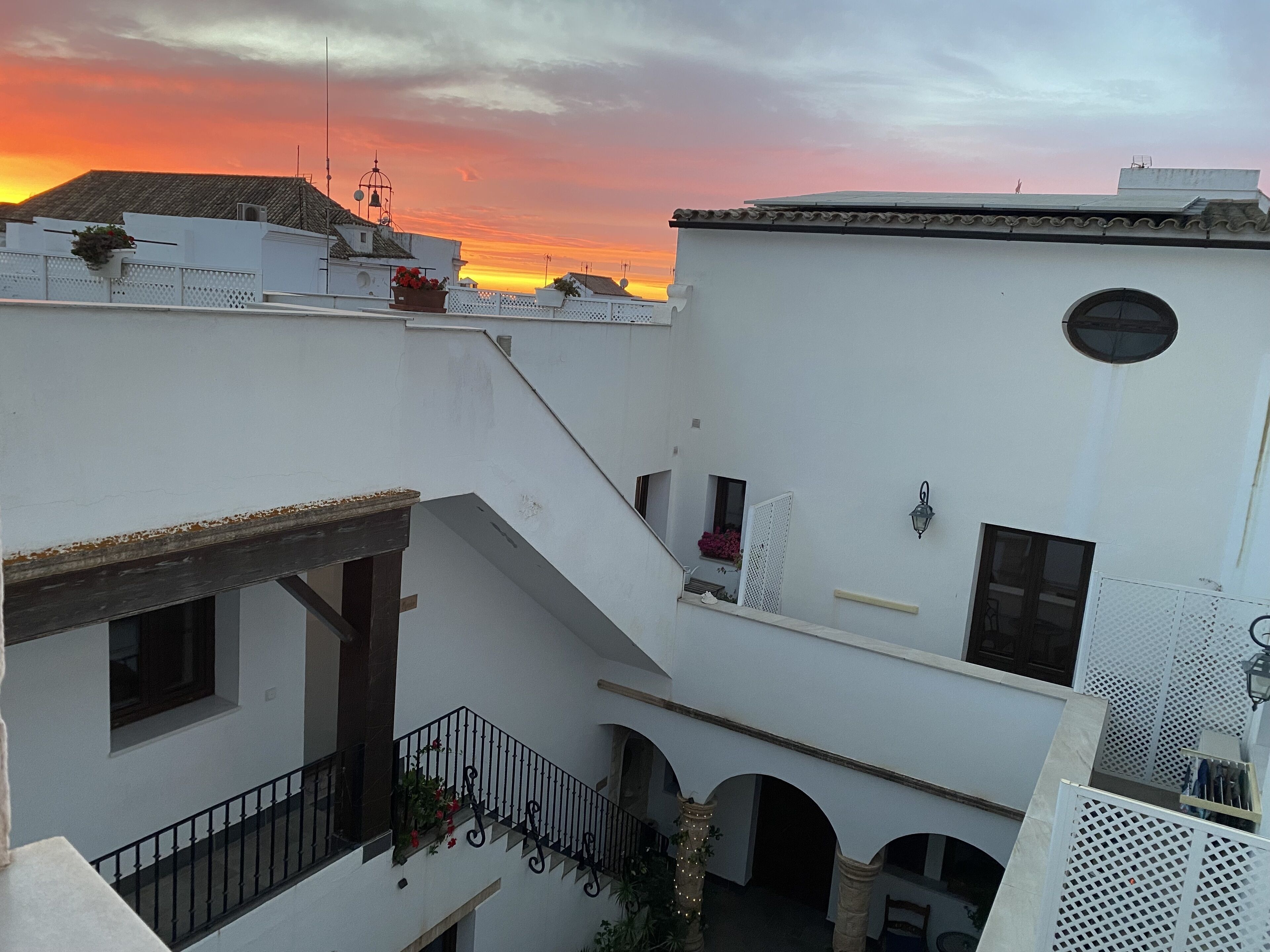 Une cour bordée de bâtiments blancs, un escalier et une vue sur le coucher de soleil.