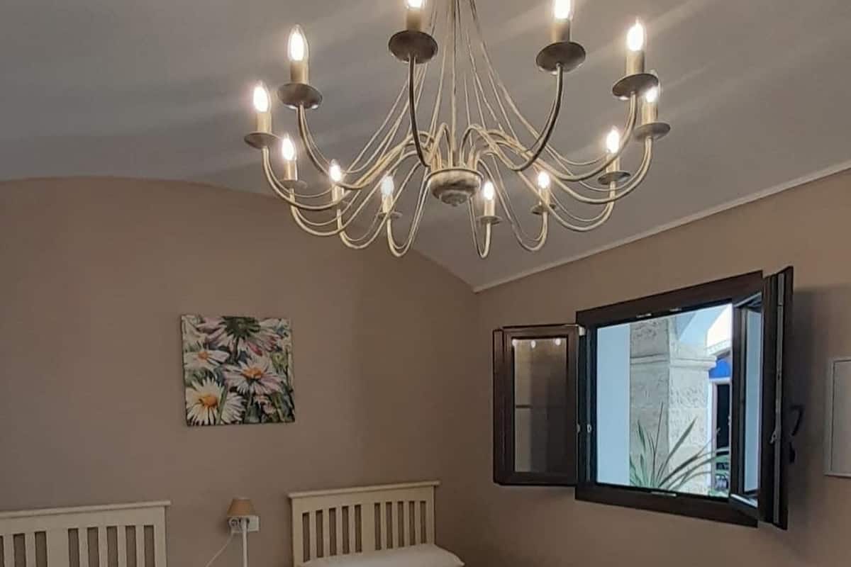 A bedroom with two beds, a chandelier, a bedside table with a lamp, a small round table, and a mirror on the wall.