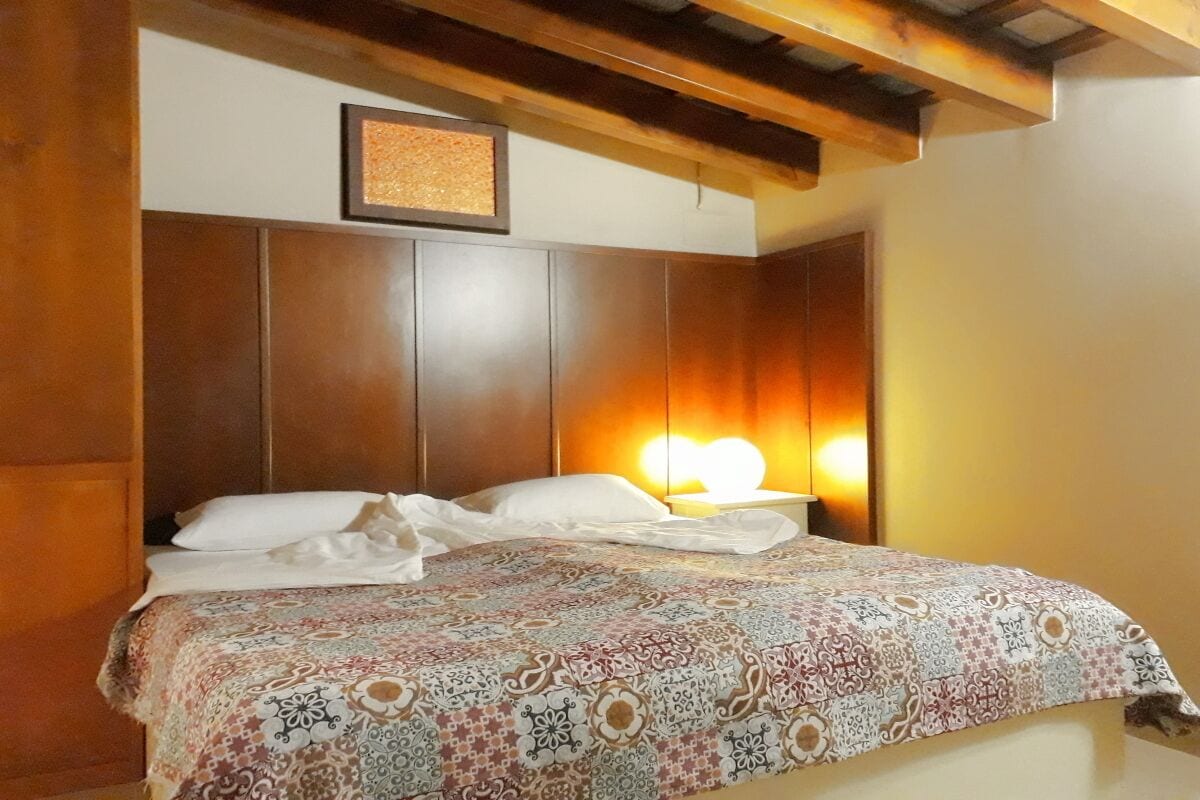 A bedroom with a wooden headboard, a patterned bedspread, and a bedside lamp.