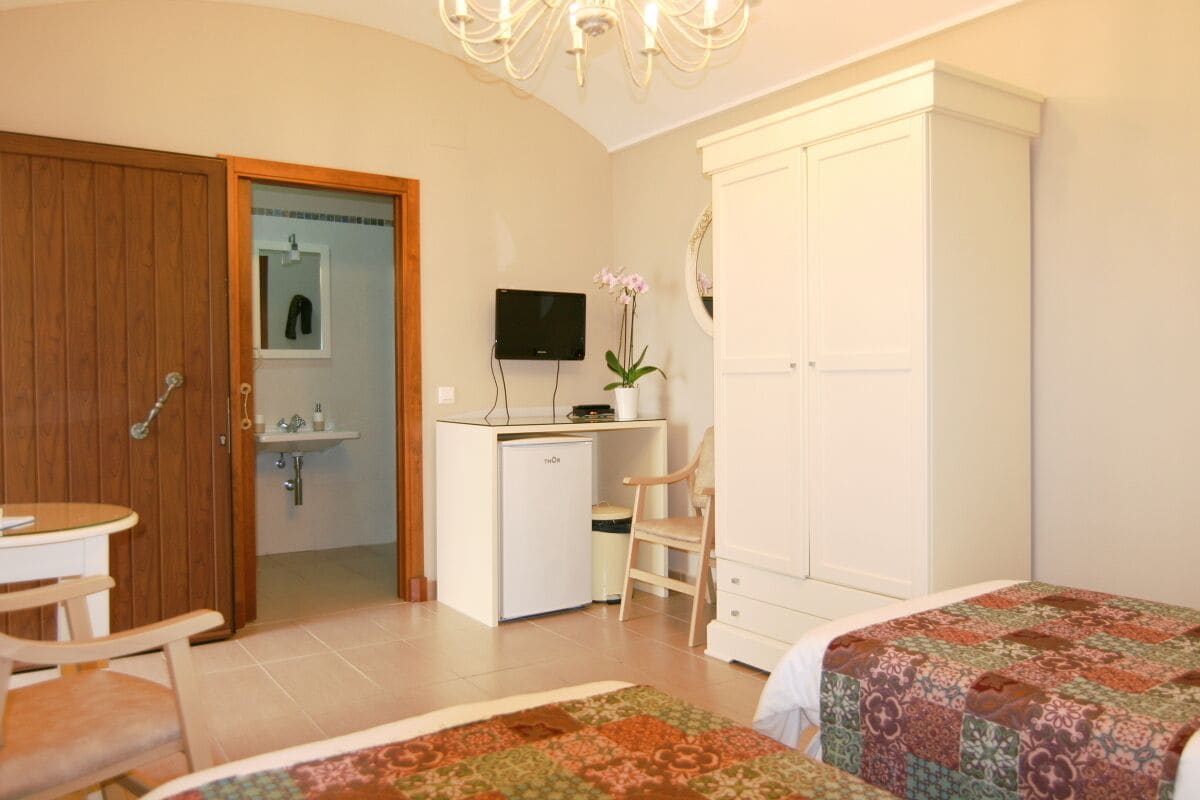 A bedroom with a bed, a desk, a chair, a wardrobe, and a television.
