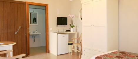 A bedroom with a bed, a desk, a chair, a wardrobe, and a television.