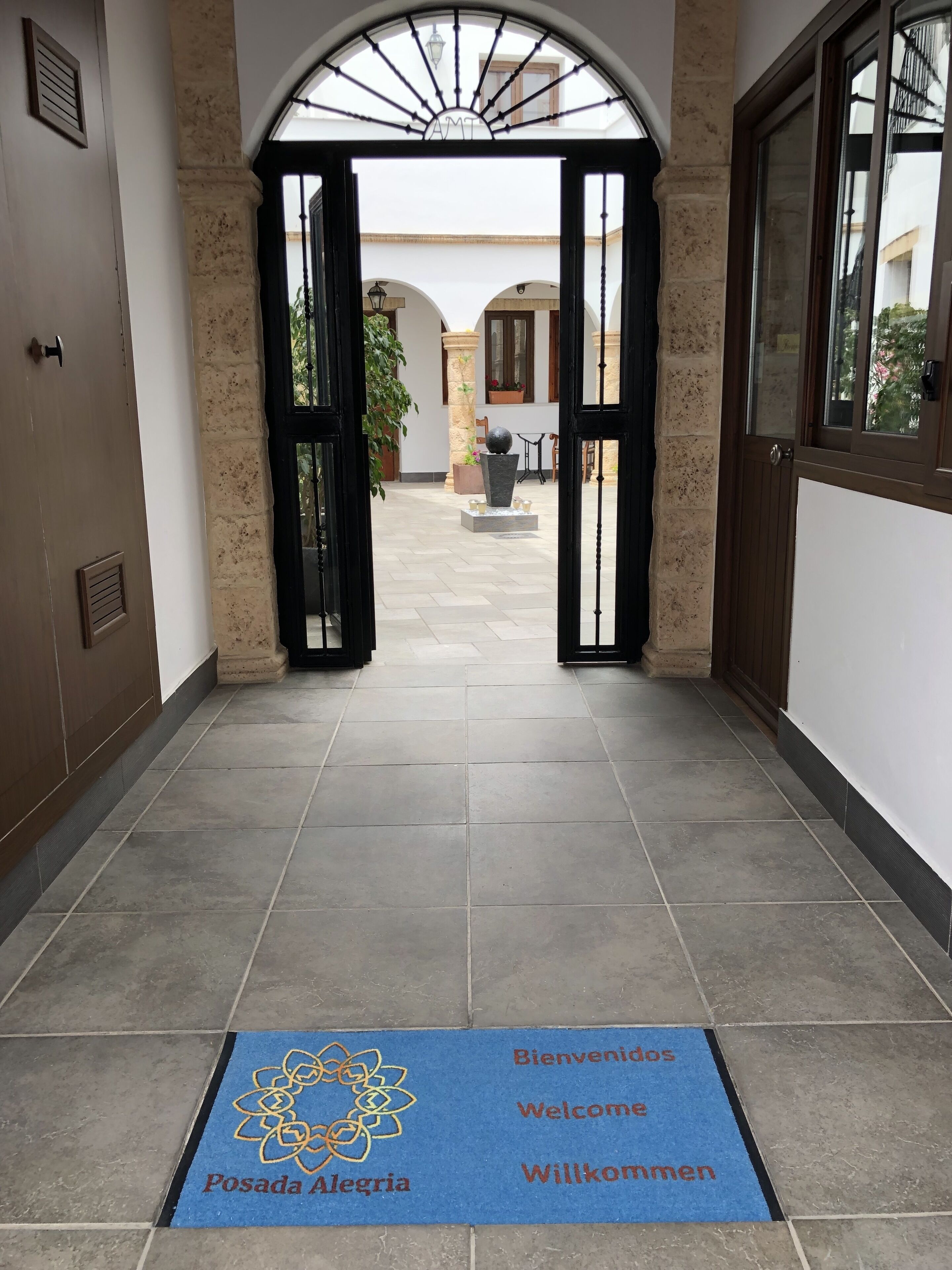 Entrada de un hotel con un felpudo azul, piso de baldosas y vistas al patio.