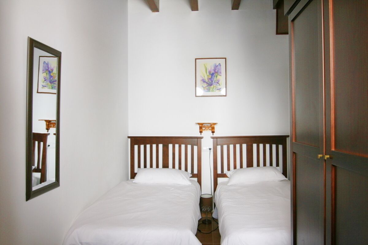 Une chambre avec deux lits simples, une tête de lit en bois, un miroir et un tableau encadré au mur.