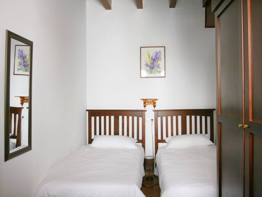 Une chambre avec deux lits simples, une tête de lit en bois, un miroir et un tableau encadré au mur.
