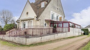 A two-story house with a stone facade, a red balcony, and a fenced front yard.